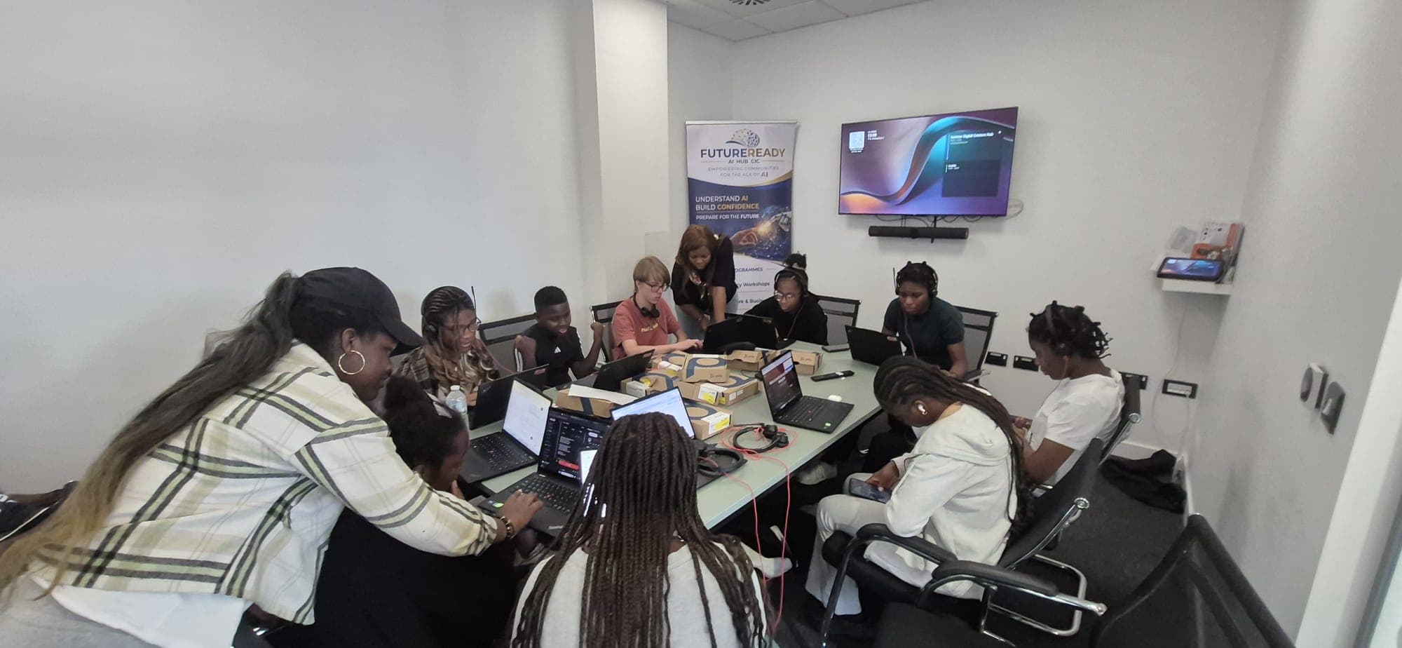 Young people working on laptops around a table with a trainer supporting them at the digital hub