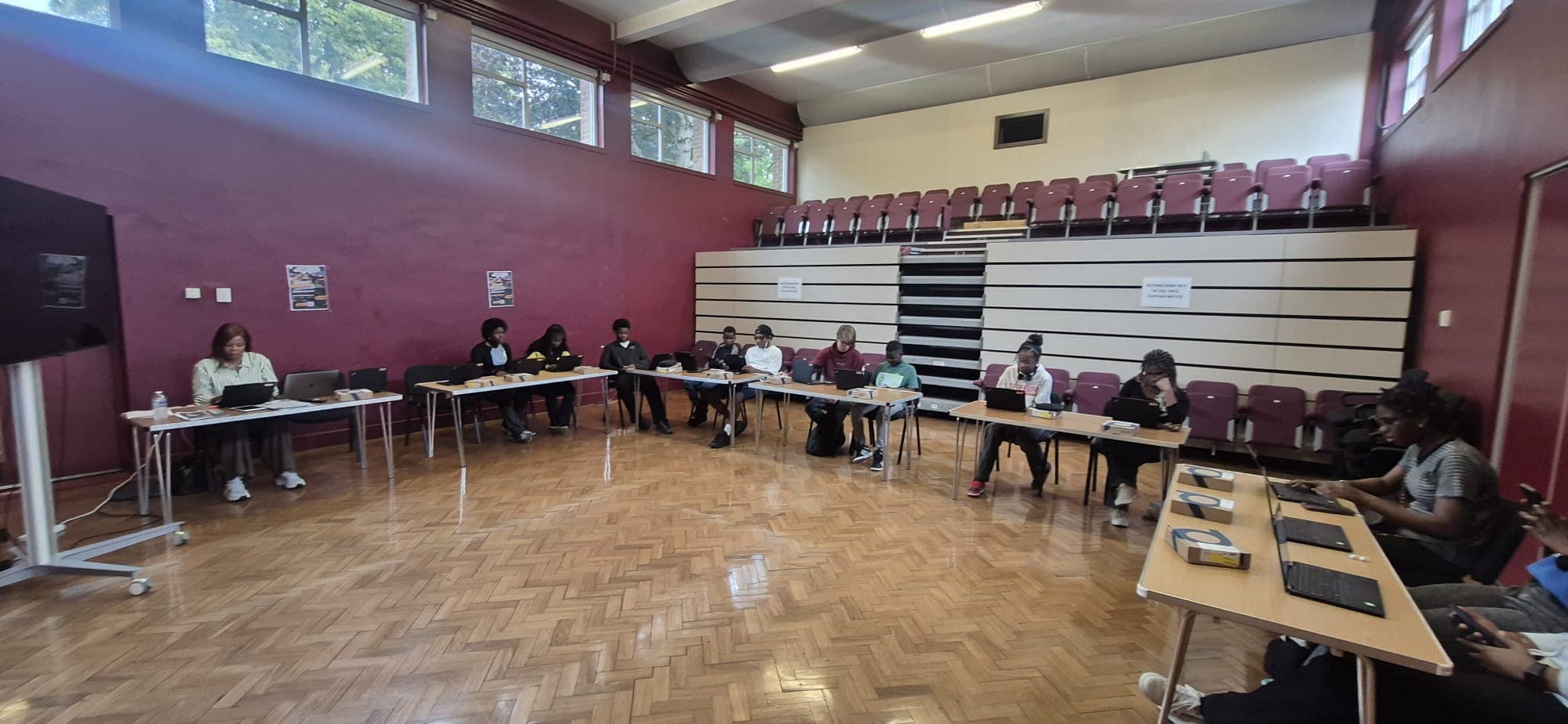 A workshop running in a school hall, with participants spread across tables working on laptops